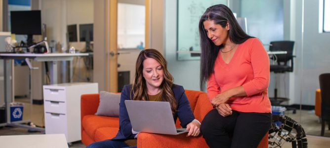 Two women in an office looking at a laptop.